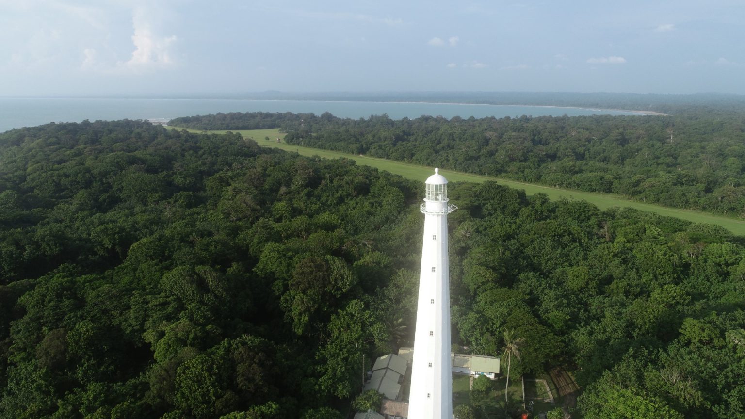 Aerial view of the Vlakkenhoek Lighthouse rising from the rainforest canopy at Tambling, with the coastline and sea beyond